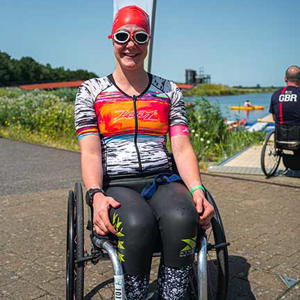 athlete smiling in wheelchair with swim hat, goggles and wetsuit on