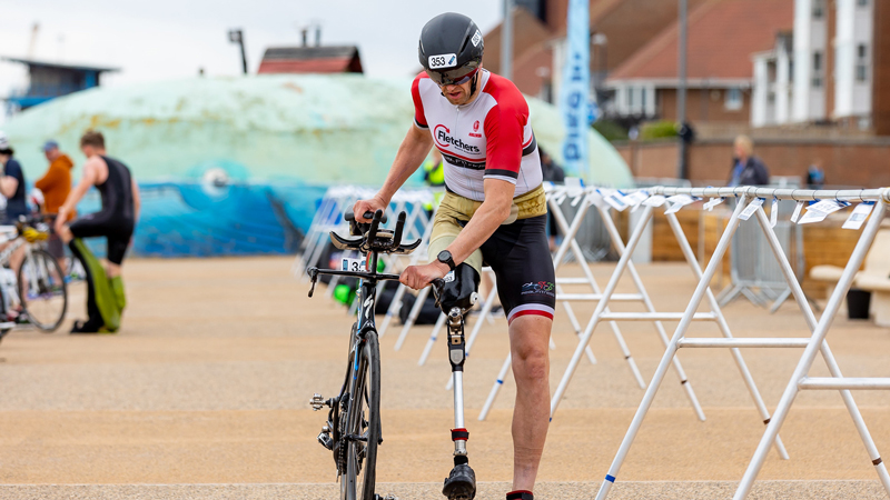 A paratriathlete with a leg impairment pushes their bike through transition at an event.