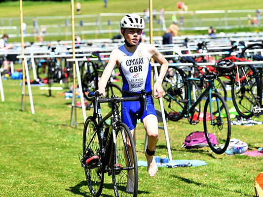 boy running with bike and helmet on out of the transition area
