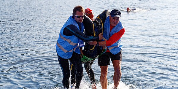 two men helping to carry a paratriathlete out of the water