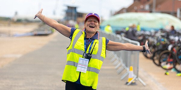 woman in high vis vest smiling with arms outstretched with joy at the camera