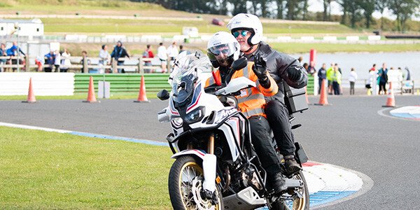 two male technical officials on a motorbike riding around the bike course of an event