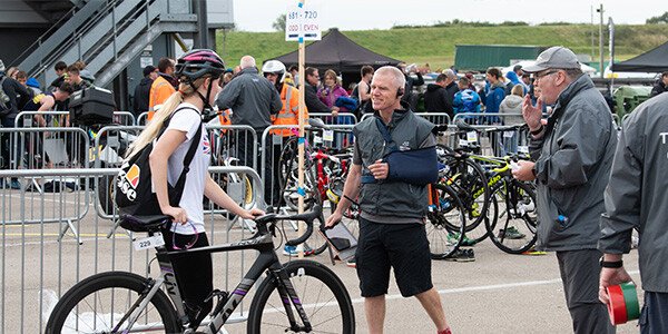 two male technical officials checking in a participant with their bike and helmet on into the transition area